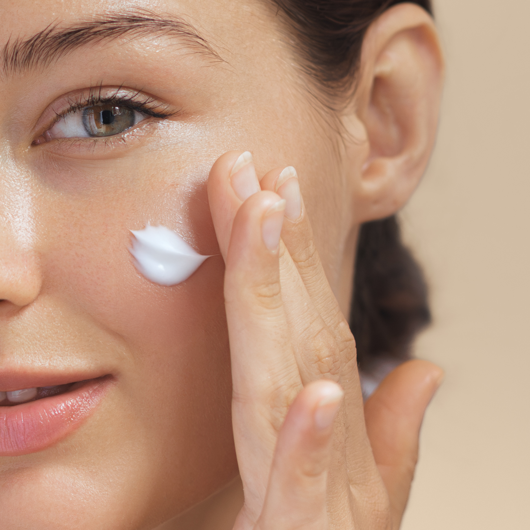 Woman applying cream to her face with a neutral background